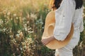 Stylish boho woman walking with straw hat in hand close up among wildflowers in sunset light. Atmospheric moment. Summer travel. Royalty Free Stock Photo