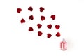 Stylish bottle of perfume with spray of vibrant red heart-shaped confetti on white background. Creative trendy flat lay