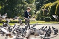 Stylish boy  in the park feeds pigeons. There are a lot of birds. Baby happy feed hungry pigeons Royalty Free Stock Photo