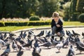 Stylish boy in the park feeds pigeons. There are a lot of birds. Baby happy feed hungry pigeons