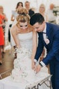 Stylish bride and groom cutting together amazing beautiful wedding cake decorated with flowers at wedding reception in restaurant Royalty Free Stock Photo