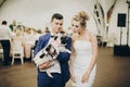 Stylish bride and groom hugging and having fun with pug dog in bow tie at wedding reception. Happy wedding couple with their dog Royalty Free Stock Photo