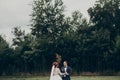 Stylish bride and groom walking and smiling on background green trees, holding hands. luxury wedding couple newlyweds dancing,
