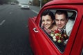 Stylish bride and happy groom looking out of driving  retro car, having fun and kissing Royalty Free Stock Photo