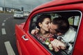 Stylish bride and happy groom looking out of driving  retro car, having fun and kissing Royalty Free Stock Photo