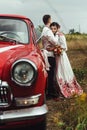 Stylish bride and happy groom near red retro car on the background of nature Royalty Free Stock Photo