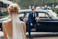 Stylish bride looking at happy groom,  walking to her from car. luxury wedding couple first looks, embracing in city street. Royalty Free Stock Photo