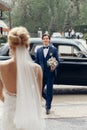 Stylish bride looking at happy groom,  walking to her from car. luxury wedding couple first looks, embracing in city street. Royalty Free Stock Photo