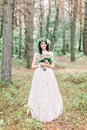 Stylish bride posing with bouquet on background of forest, luxury gorgeous boho wedding at forest outdoors