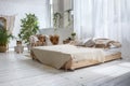 Stylish bright loft cozy room with double bed, armchair, green plants, curtains, white brick walls and wooden floor