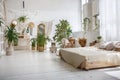 Stylish bright loft cozy room with double bed, armchair, green plants, mirror, white brick walls and wooden floor