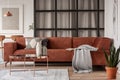 Stylish brown corner sofa with patterned pillows in elegant living room interior with mullions wall