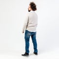 Stylish brown-haired curly guy with a beard dressed in beige jumper over a white shirt and jeans poses in the studio on Royalty Free Stock Photo