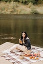 brunette girl in a leather jacket drinks tea from a mug on the lakeside picnic