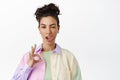 Stylish brunette girl show tongue, wink and okay OK sign, have zero problems, all under control, standing against white Royalty Free Stock Photo