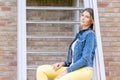 Stylish brunette girl wearing jeans vest, white t-shirt and yellow jeans posing against stairs in the city , urban Royalty Free Stock Photo