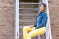 Stylish brunette girl wearing jeans vest, white t-shirt and yellow jeans posing against street , urban clothing style Royalty Free Stock Photo