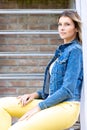 Stylish brunette girl wearing jeans vest, white t-shirt and yellow jeans posing against street , urban clothing style Royalty Free Stock Photo