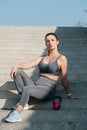 Stylish brunette sitting on the long stairs outdoors, posing with a kettlebell Royalty Free Stock Photo