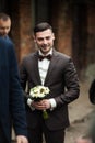Stylish brunette smiling groom in a suit with a brown bow holds Royalty Free Stock Photo