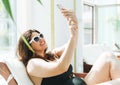 Stylish brunette woman plus size body positive in black swimsuit and sunglasses taking selfie on mobile phone on lounger in spa Royalty Free Stock Photo