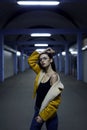 Stylish brunette in yellow jacket, jeans and glasses for womenswear fashion photo shoot. City lights by night