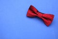 Stylish burgundy bow tie with polka dot pattern on blue background, top view. Space for text
