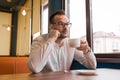 Stylish business businessman with a misunderstood expression speaks on his smartphone and drinks coffee sitting at a table in a