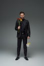 Stylish businessman holding flowers and basket with fruits on grey, international womens