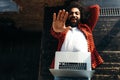 Stylish businessman lies on a sofa with a laptop looking at the camera and raising his hand up Royalty Free Stock Photo