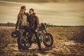 Stylish cafe racer couple on the vintage custom motorcycles in a field. Royalty Free Stock Photo