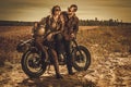 Stylish cafe racer couple on the vintage custom motorcycles in a field.