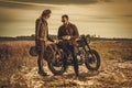 Stylish cafe racer couple on the vintage custom motorcycles in a field.