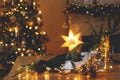 Stylish candle, golden lights, pine cones and ornaments on wooden table against stylish decorated christmas tree and fireplace