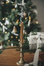 Stylish candle, wrapped christmas gift, rustic basket with fir branches against festive decorated tree in scandinavian room. Merry