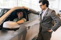 Stylish car dealer wearing business suit talking to young man client sitting in car salon. Professional salesman helping