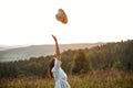 Stylish carefree boho girl throwing her hat in the sky in sunny light  at atmospheric sunset. Happy hipster woman in linen rustic Royalty Free Stock Photo