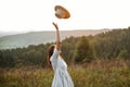 Stylish carefree boho girl throwing her hat in the sky in sunny light  at atmospheric sunset. Happy hipster woman in linen rustic Royalty Free Stock Photo