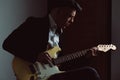 Stylish caucasian man sitting on chair playing electric guitar at home. Home leisure, music performance. Self-isolation concept. Royalty Free Stock Photo