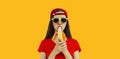 Stylish caucasian young woman eating banana wearing red baseball cap on orange background Royalty Free Stock Photo