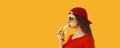 Stylish caucasian young woman eating banana wearing red baseball cap on orange background Royalty Free Stock Photo