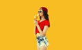 Stylish caucasian young woman eating banana wearing red baseball cap on orange background Royalty Free Stock Photo