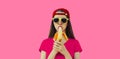 Stylish caucasian young woman eating banana wearing red baseball cap on pink background Royalty Free Stock Photo