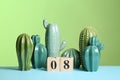 Stylish ceramic cactuses and wooden block calendar on table against color background.
