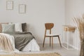 Stylish chair next to warm king size bed in scandinavian bedroom