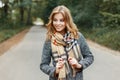 Stylish cheerful European young woman with a cute smile in a fashionable gray coat in a vintage beige checkered scarf Royalty Free Stock Photo