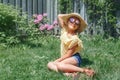 Stylish child girl in sunglasses and straw hat sitting on grass outdoors. Happy smiling Caucasian kid having fun at home backyard Royalty Free Stock Photo