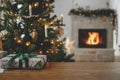 Stylish christmas gift close up against decorated tree and burning fireplace. Merry Christmas! Beautiful modern wrapped present