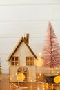 Stylish christmas house and glitter christmas tree in golden lights. Modern festive decor in scandinavian room. Miniature village