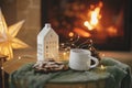 Stylish christmas little house with golden lights, gingerbread cookies and tea cup on table on background of fireplace in festive Royalty Free Stock Photo